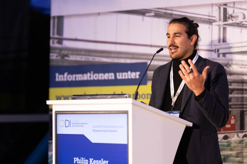 Mann stehend gestikuliert hinter einem Podium auf einer Bühne