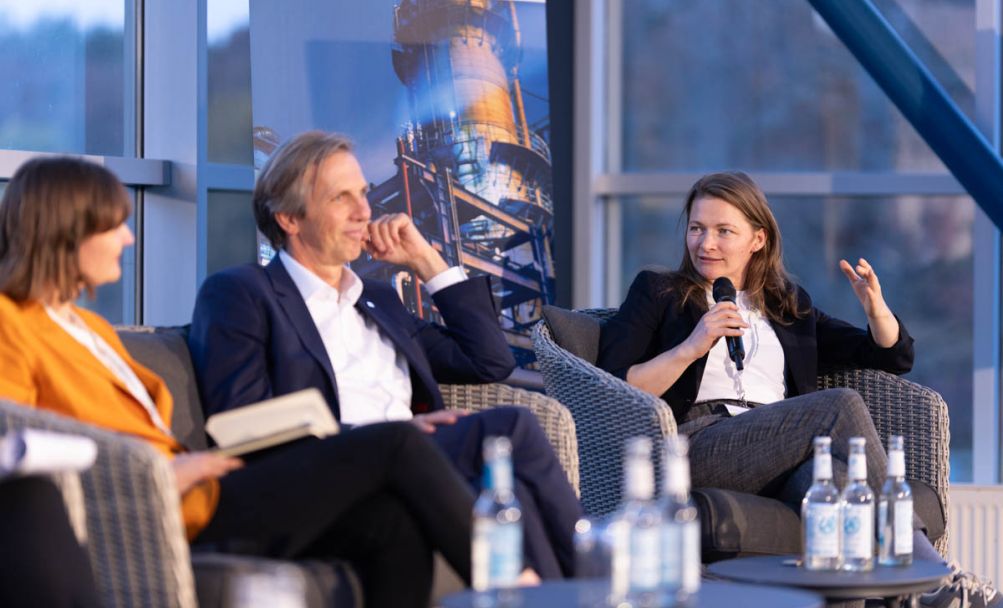 Drei Personen sitzen nebeneinander und unterhalten sich auf einer Bühne