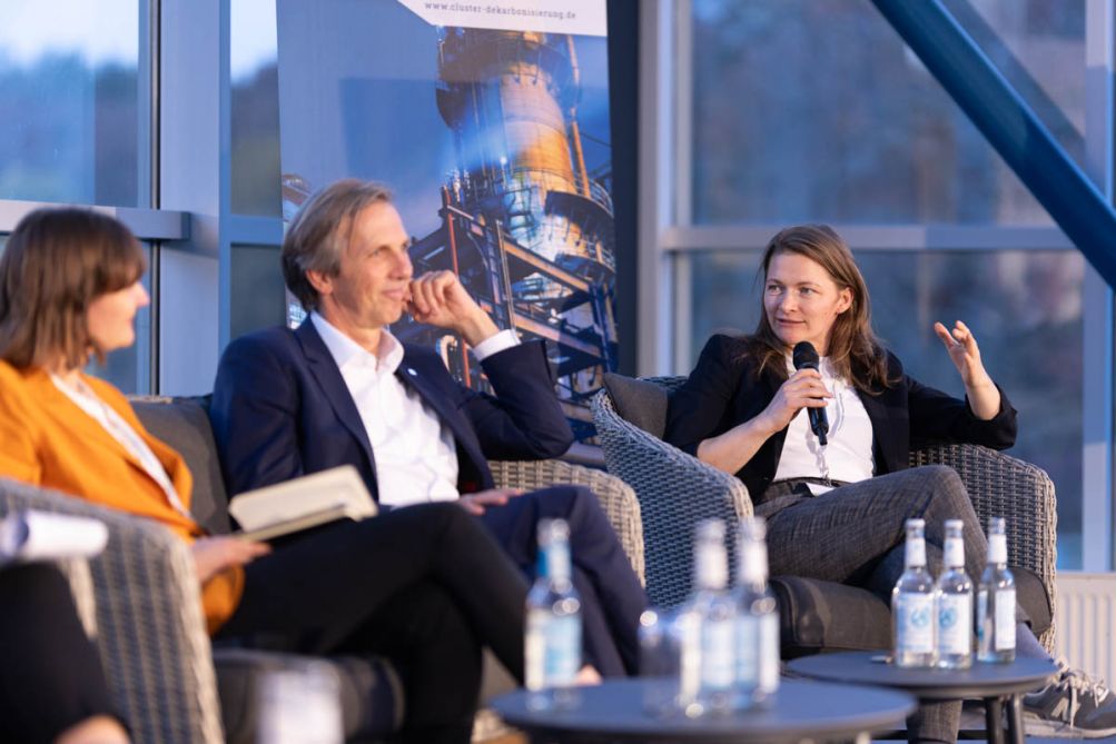 Drei Personen sitzen nebeneinander und unterhalten sich auf einer Bühne