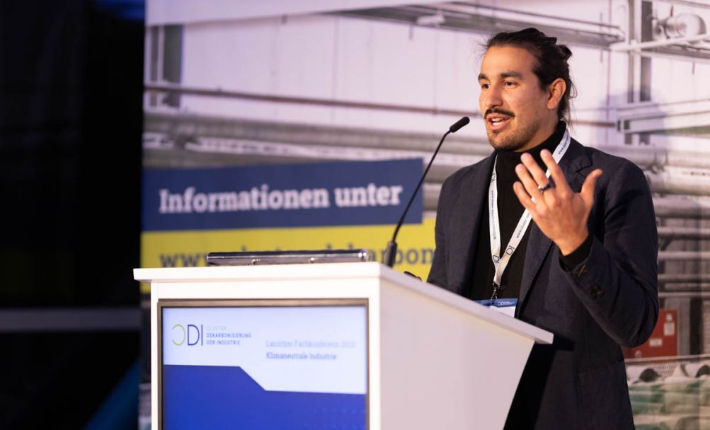 Mann stehend gestikuliert hinter einem Podium auf einer Bühne