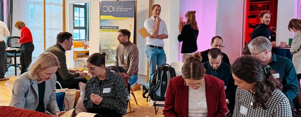 Menschen sitzen etwas verteilt im Raum und unterhalten sich