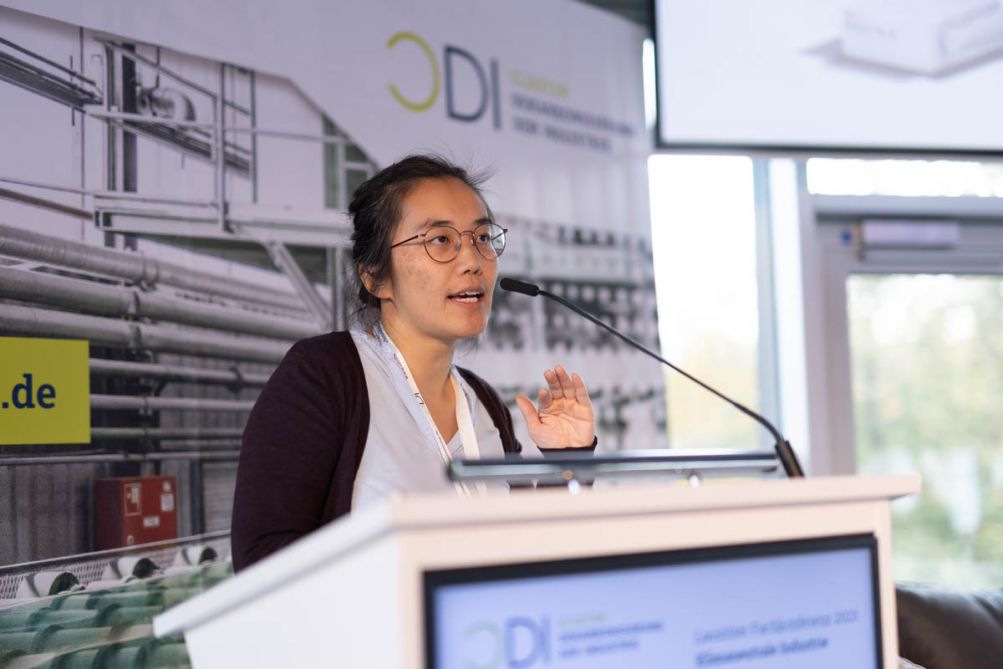 Frau stehend gestikuliert hinter einem Podium auf einer Bühne