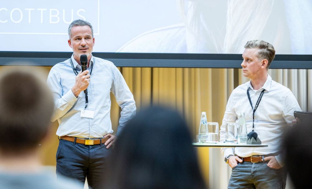 Rico Schneider spricht zum Publikum, Erik Blasius steht daneben