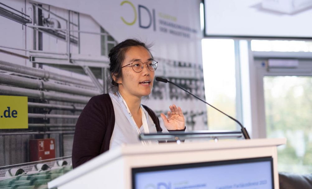 Frau stehend gestikuliert hinter einem Podium auf einer Bühne