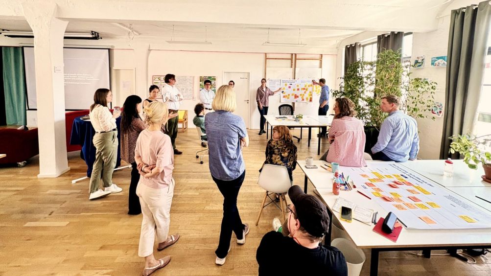 Menschen in Workshopumgebung stehen vor einem Whiteboard