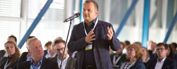 Mann vor Mikrofon mit Publikum im Hintergrund